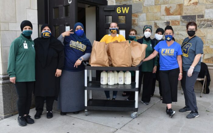 Food workers at Fordson High School stand around the student milk and bags of food waiting to be distributed for student meals on June 9, 2021.