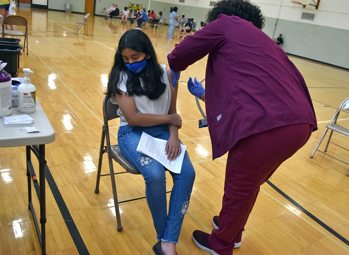 A girl looks away while getting her COVID vaccination at Edsel Ford High School in May.