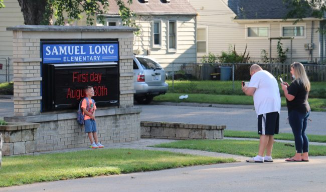 A student stands in front of the Long Elementary School sign to pose for a picture on the first day of school in August 2021.