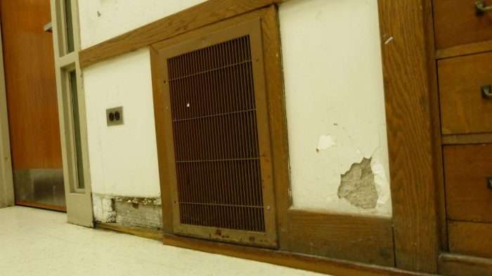 Chipped plaster on a wall and missing and damaged baseboard in a school