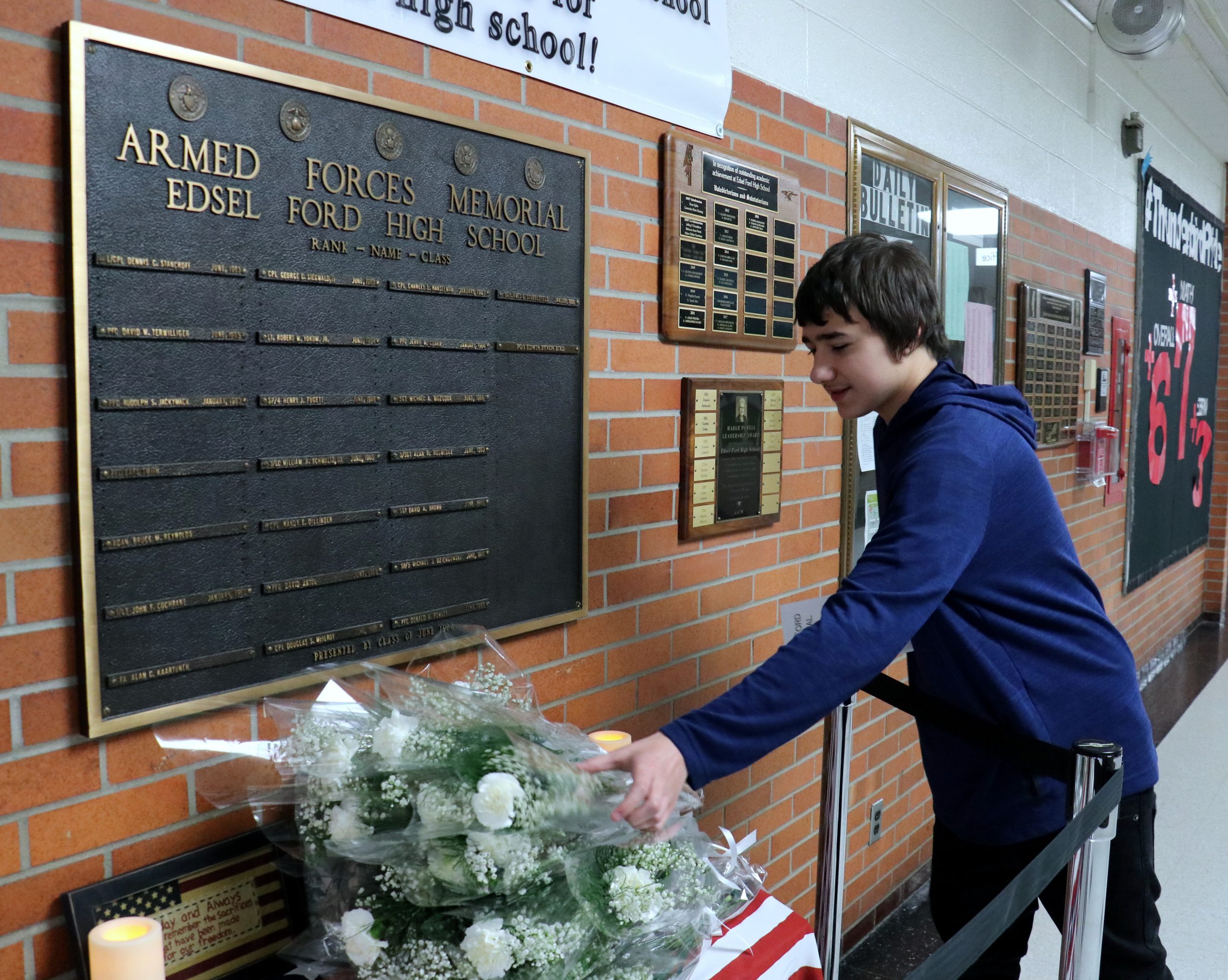 During the 2018 Memorial Day ceremony at Edsel Ford High School, a student lays flowers before a plaque remembering former students who died in service.