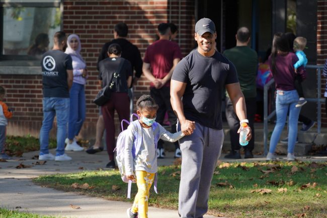 A man smiles while holding a young girl's hand and walking outside of Haigh Elementary School in the fall of 2021.