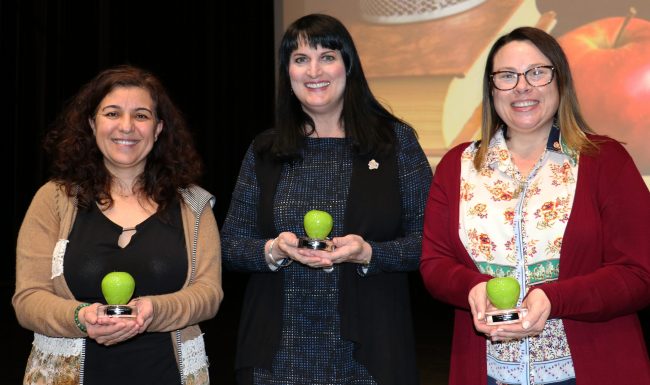 Three women Teacher of the Year awards shaped like glass apples.