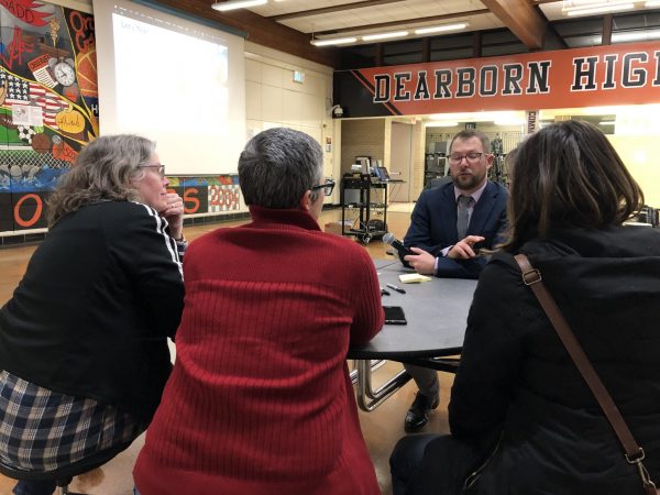 Four people sit and talk around a table at Dearborn High School during a special town hall meeting.