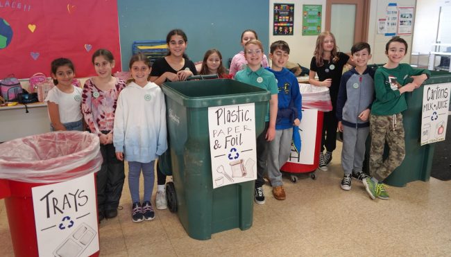 Eleven students stand by recycling containers to help students recycle school lunch waste.