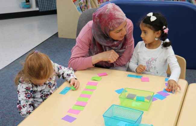 An adult works with two young students using slips of paper to show color patterns at Cotter Early Childhood Center in the spring of 2023.