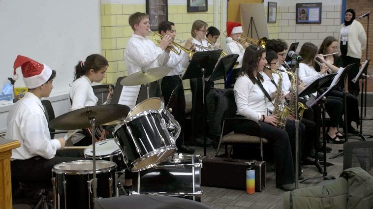About a dozen middle school student musicians and one teacher play musical instruments during a school board meeting.