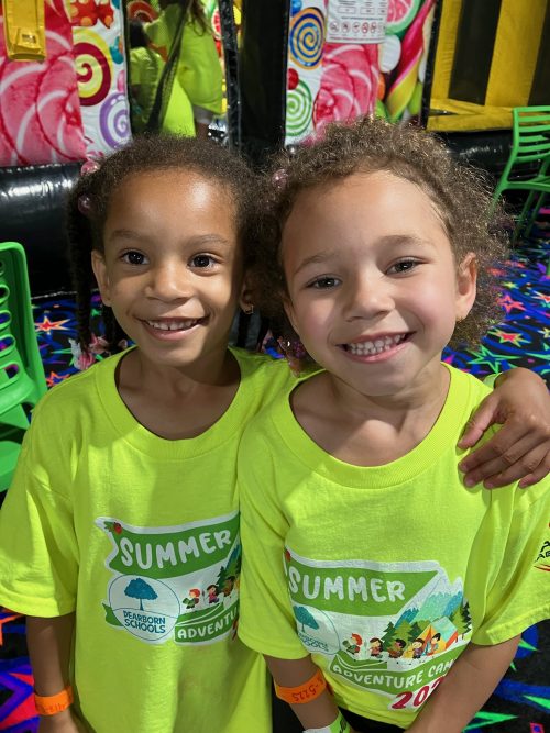 Two children smile while wearing bright Summer Adventure Club shirts
