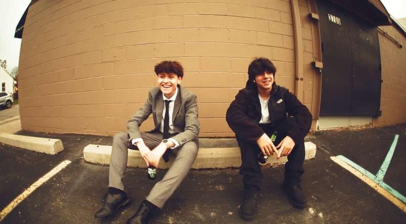 Two young men sit on a curb in a still from the movie "Head for the Truth."