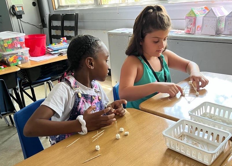 Two students work on creating a structure from toothpicks and mini marshmallows.
