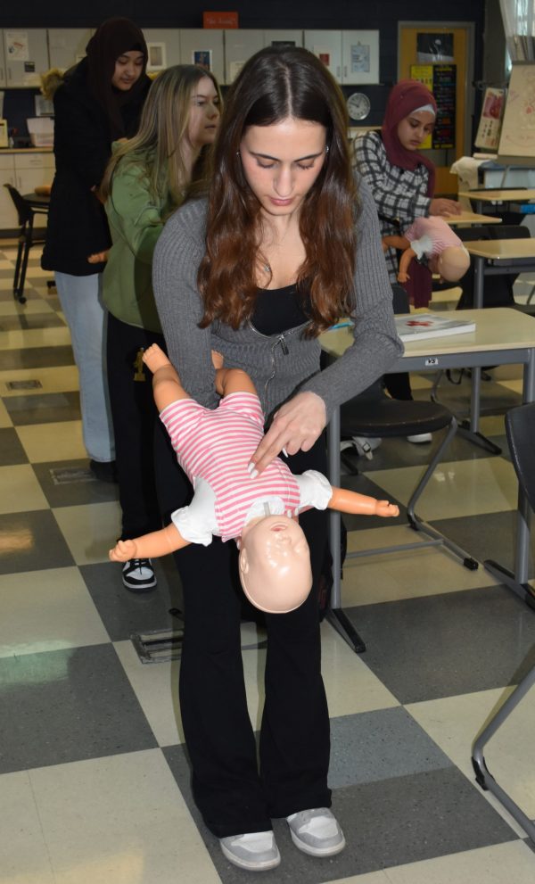 PR 25 Choking infant first aid MBCC A teen holds a baby medical mannequin upside down as she practices treating an infant for choking