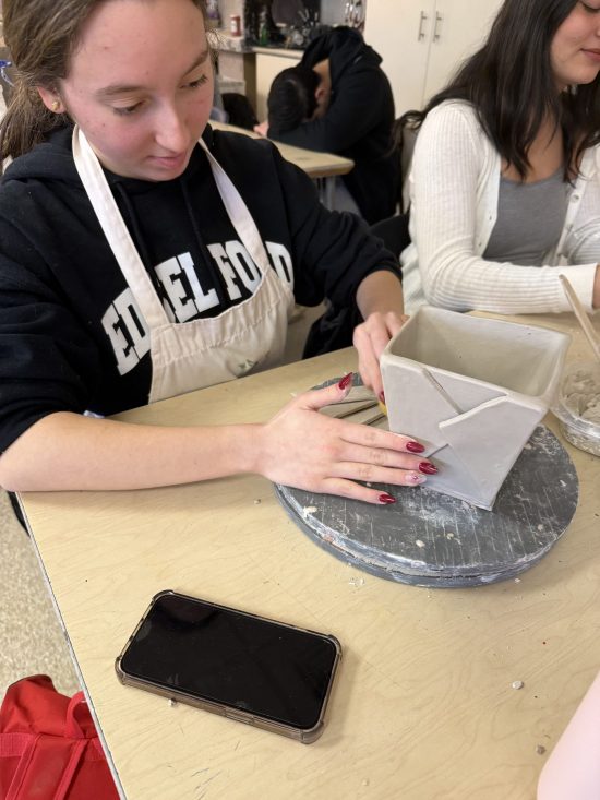 A student in an Edsel Ford shirt makes a clay sculpture.