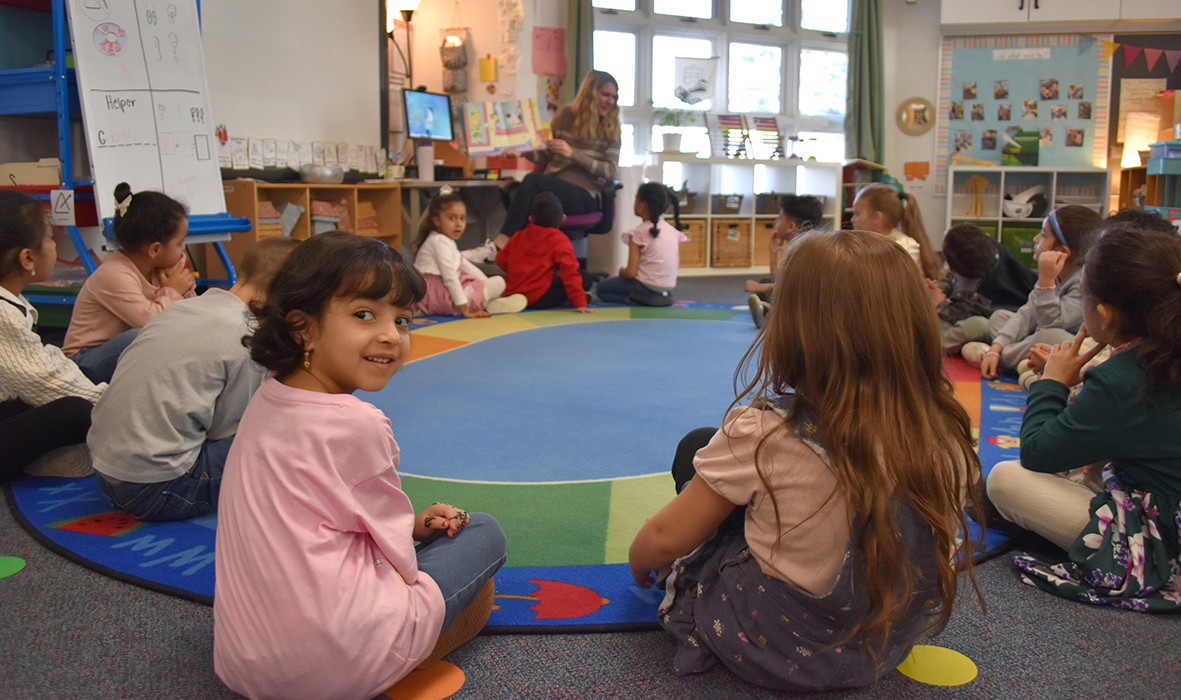 GSRP story time smaller Students site in a circle on the floor listening to a teacher read a story.